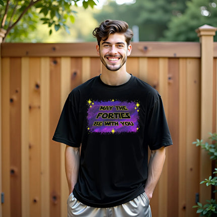 Man wearing ‘May the Forties Be With You’ black birthday t-shirt outdoors, retro yellow lettering on blue-purple galaxy background, playful and confident 40th birthday celebration vibe.