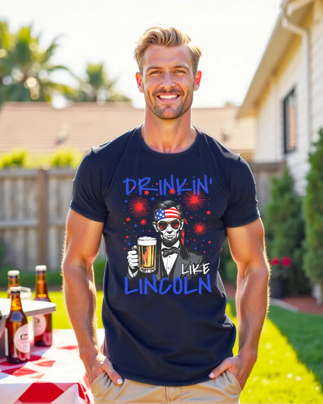 Male model wearing navy ‘Drinkin Like Lincoln’ t-shirt at July 4th BBQ featuring Abraham Lincoln graphic with flag bandana, sunglasses, and beer mug design, patriotic-inspired summer apparel.