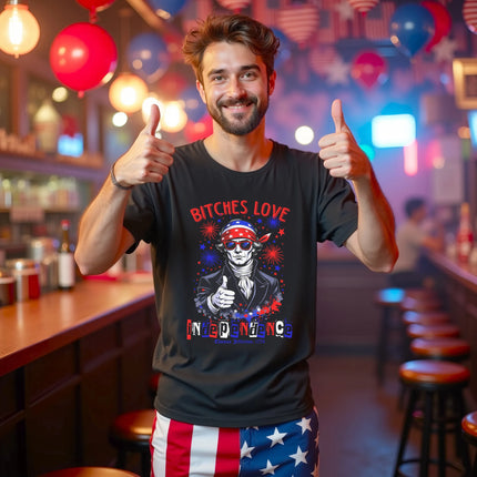 Male model wearing black ‘Bitches Love Independence’ t-shirt at the bar, Jefferson in sunglasses with fireworks graphic, edgy and playful July 4th vibe.