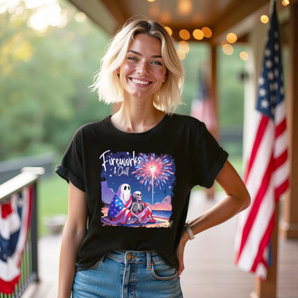 Female model wearing black ‘Fireworks and Chill’ t-shirt outdoors, cute ghost and skeleton couple with fireworks beach scene, cozy and playful July 4th vibe