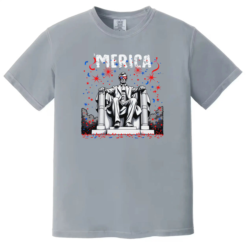 Funny Independence Day shirt in gray, featuring Lincoln in seated pose with flag sunglasses and fireworks, bold ‘Merica graphic tee.