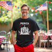 Male model wearing black ‘Merica t-shirt outdoors, Abraham Lincoln seated graphic with flag sunglasses and fireworks, relaxed July 4th BBQ vibe.