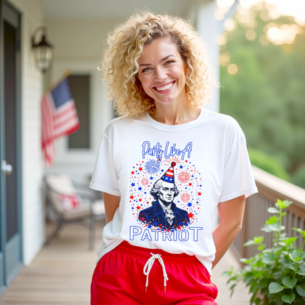 Female model wearing white ‘Party Like a Patriot’ t-shirt outdoors, George Washington bust with party hat and fireworks, fun July 4th party vibe.