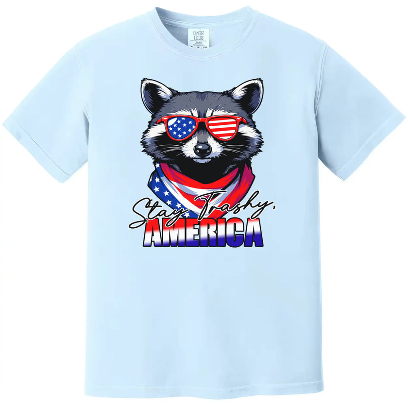 Patriotic raccoon graphic tee in light blue, ‘Stay Trashy America’ design with sunglasses and bandana, fun Independence Day shirt.