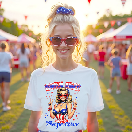 Female model wearing white ‘Born Free But Now I’m Expensive’ t-shirt, retro pinup girl with patriotic outfit and sunglasses, confident July 4th party vibe.