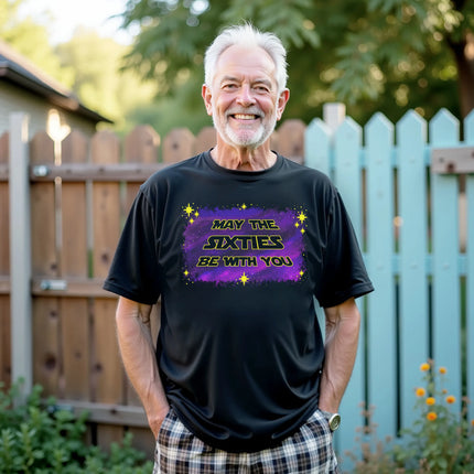 Model wearing black “May the Sixties Be With You” birthday t-shirt in casual lifestyle setting showing retro galaxy lettering and starry background design