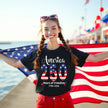 Female model wearing black America 250 years of freedom t-shirt outdoors, flag-filled 250 design with star sparkles, patriotic celebration vibe.
