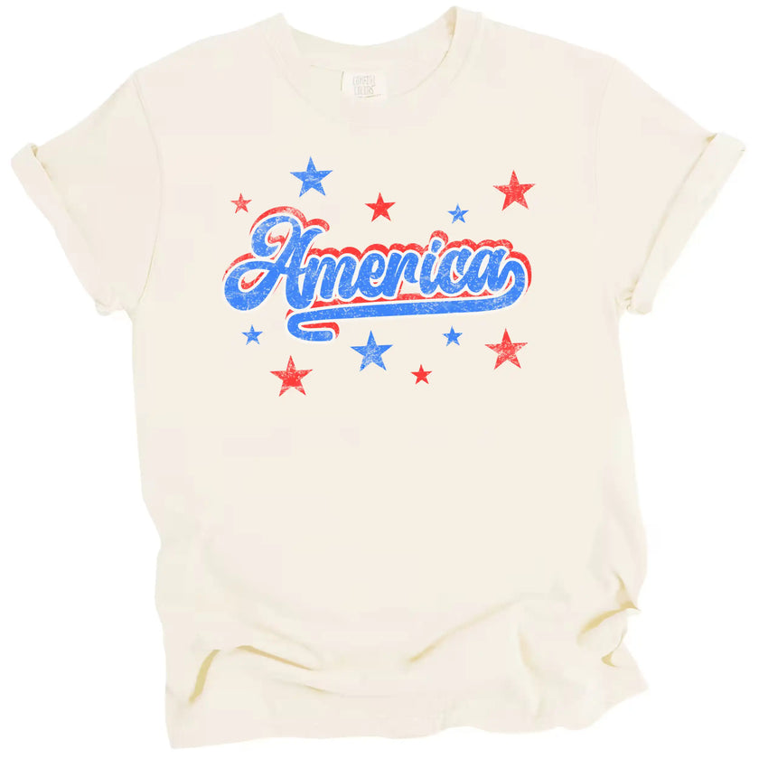 Vintage patriotic America tee in cream, distressed lettering with bold red white blue outline and subtle star sparkle accents.