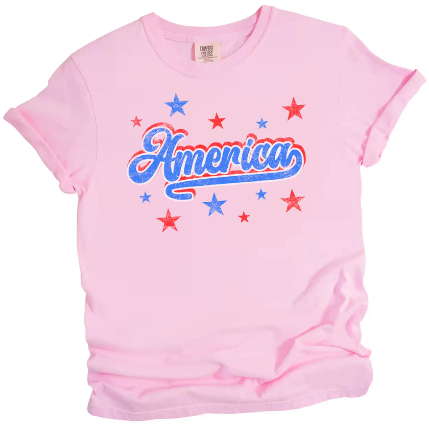 Cute vintage America shirt in pink, distressed red white blue lettering with bold outlines and star sparkle details, retro July 4th tee.