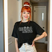 Female model wearing black ‘Aspiring Retiree’ t-shirt outdoors, retro vintage lettering design, funny sarcastic casual vibe.