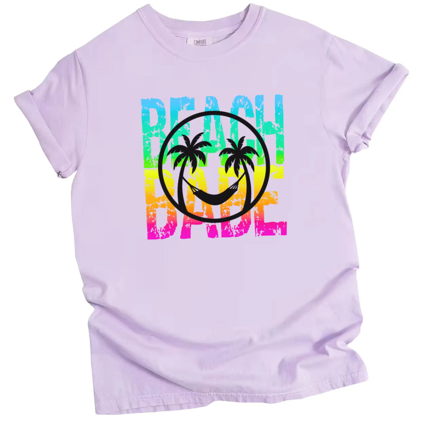Beach Babe t-shirt in light purple, neon rainbow distressed lettering with beach smile face and palm tree graphic design.