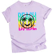 Beach Babe t-shirt in light purple, neon rainbow distressed lettering with beach smile face and palm tree graphic design.