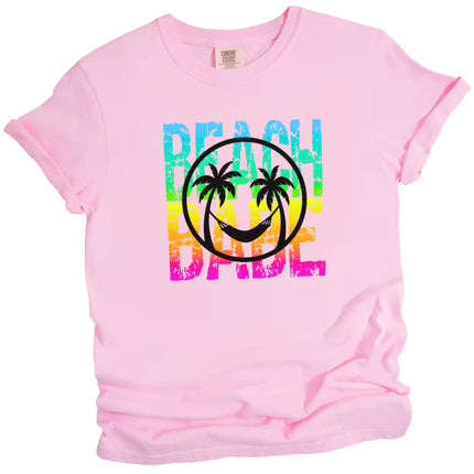 Cute summer Beach Babe shirt in pink, neon rainbow distressed text with palm tree smile face and hammock graphic design.