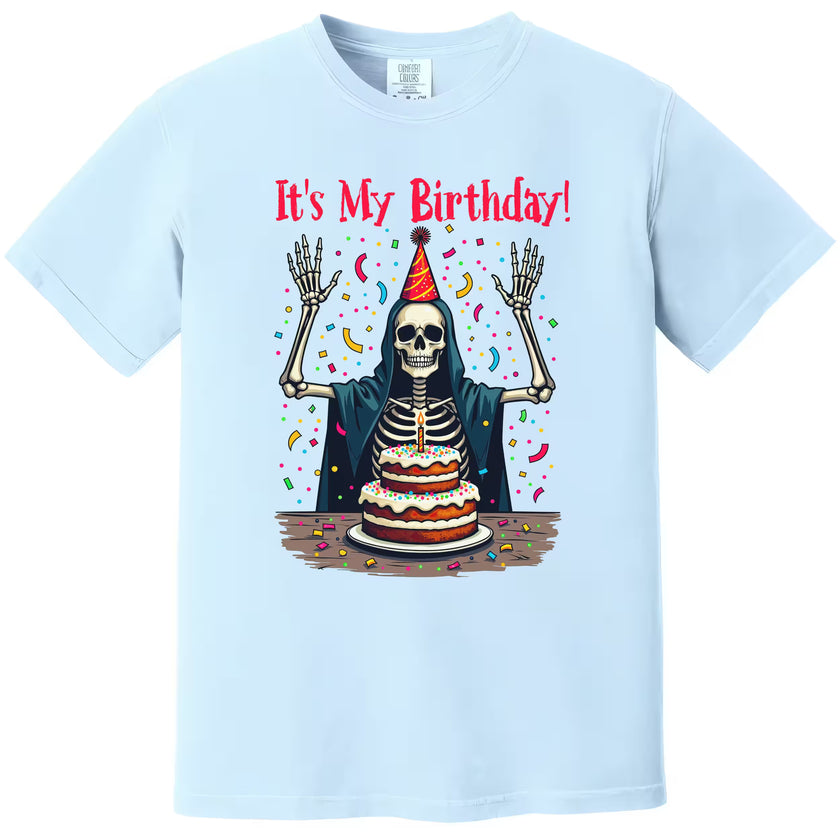 Light blue “It’s My Birthday” skeleton t-shirt flat lay featuring skeleton in party hat, cloak, and falling confetti for fun birthday vibes