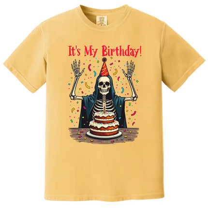Yellow “It’s My Birthday” skeleton t-shirt flat lay showcasing confetti, party hat, and cloak, perfect for celebrating birthdays