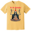 Yellow “It’s My Birthday” skeleton t-shirt flat lay showcasing confetti, party hat, and cloak, perfect for celebrating birthdays