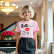 Close-up of woman wearing light pink Buffalo Girl t-shirt with magazine-style lettering, showing bold city pride and confident style.