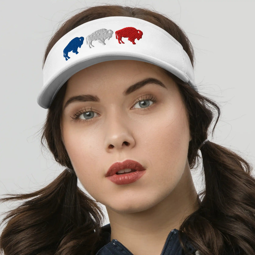 Woman wearing a white Buffalo golf visor with three embroidered buffalo silhouettes in red white and blue, a stylish athletic accessory for outdoor days.