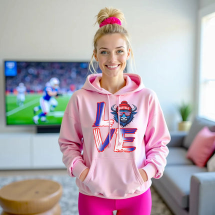 Female model wearing light pink LOVE Buffalo hoodie standing in her living room watching a football game
