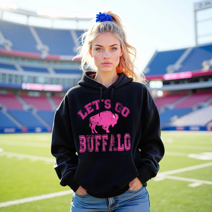 Female model wearing black Buffalo football hoodie with distressed hot pink ‘Let’s Go Buffalo’ varsity lettering and oversized pink buffalo silhouette graphic, stylish women’s game day apparel.