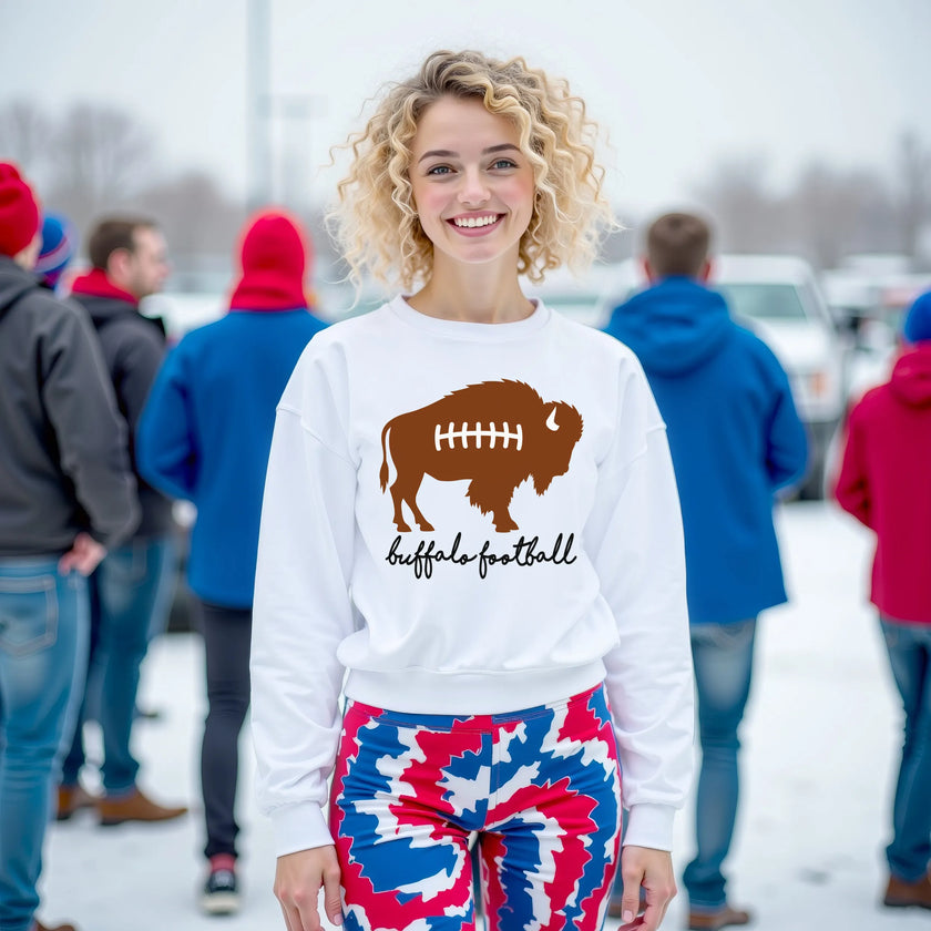 Woman wearing a white Buffalo football sweatshirt featuring a brown buffalo football graphic with laces and black scroll lettering, showing off a cute football-inspired fan look.