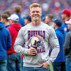 Male model wearing light gray Buffalo Football 90s retro helmet sweatshirt standing on football field drinking beer