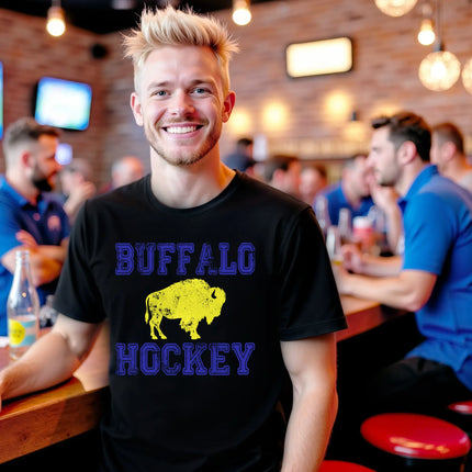Male model wearing black Buffalo hockey distressed varsity t-shirt at bar, blue lettering with yellow buffalo graphic, vintage sports fan vibe