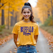Woman wearing a gold Buffalo Hockey Est. 1970 t-shirt with bold blue retro lettering, showcasing classic Buffalo hockey pride in a timeless everyday style.