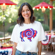 Female model wearing white Buffalo patriotic t-shirt outdoors, buffalo silhouette with red white and blue tie-dye swirl design, fun summer July 4th vibe.