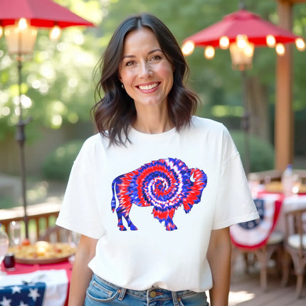 Female model wearing white Buffalo patriotic t-shirt outdoors, buffalo silhouette with red white and blue tie-dye swirl design, fun summer July 4th vibe.