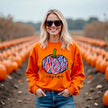 Woman wearing an orange Buffalo football Halloween sweatshirt featuring a red white and blue striped pumpkin and Let’s Go Buffalo script while enjoying a fall pumpkin patch.