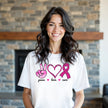 Model wearing white “Peace, Love, Cure” t-shirt in a casual lifestyle setting, confidently showing support for breast cancer awareness