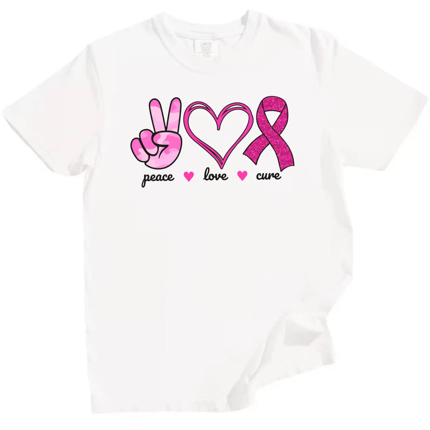 White “Peace, Love, Cure” t-shirt flat lay highlighting pink icons—peace hand, hearts, glitter ribbon—for breast cancer awareness and support