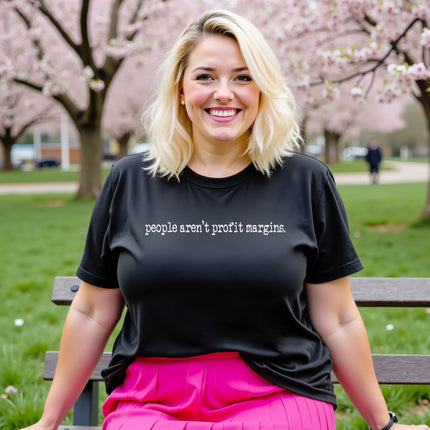 Model wearing black “People Aren’t Profit Margins” t-shirt in a casual lifestyle setting, confident and values-forward look