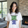 Model wearing white “Tax the Greed, Not the Need” t-shirt in a casual living room setting, confidently showing social justice and people-first values