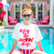 Female model wearing white Enjoy the Sweet Days strawberry t-shirt in pool, retro distressed lettering with fruit detail, cute summer vibe.
