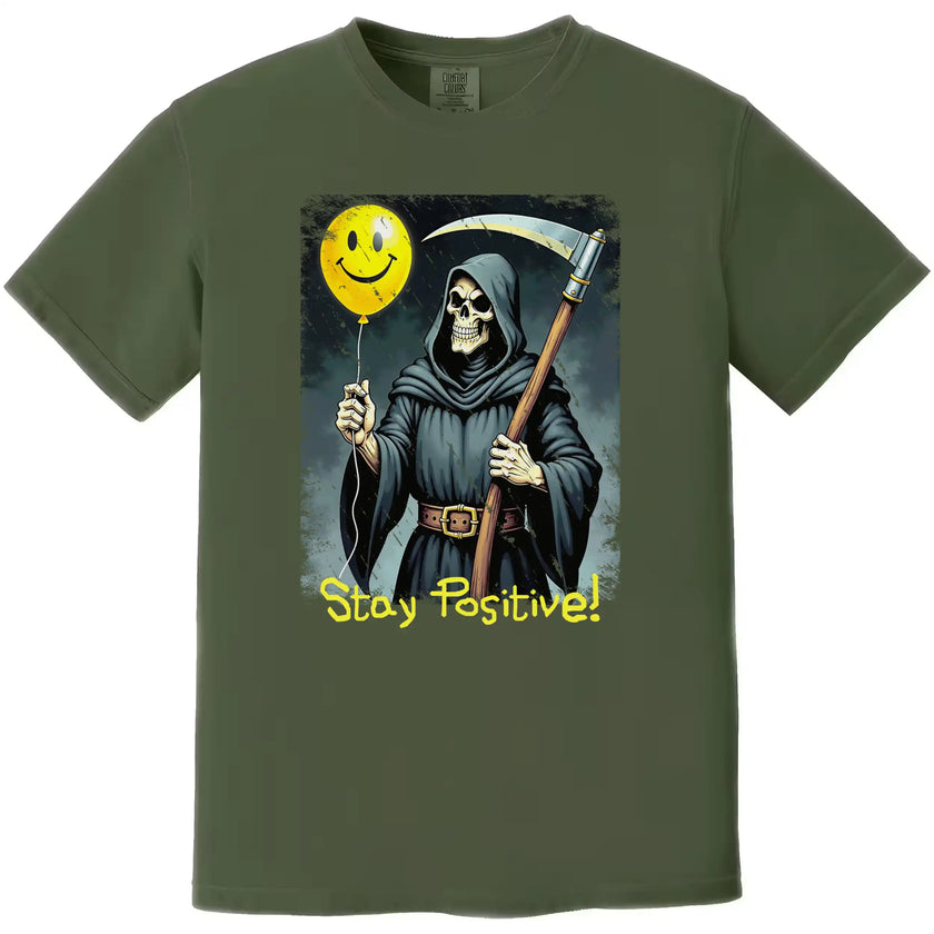 Green “Stay Positive” grim reaper t-shirt flat lay featuring sarcastic reaper graphic and bright yellow smiley balloon design