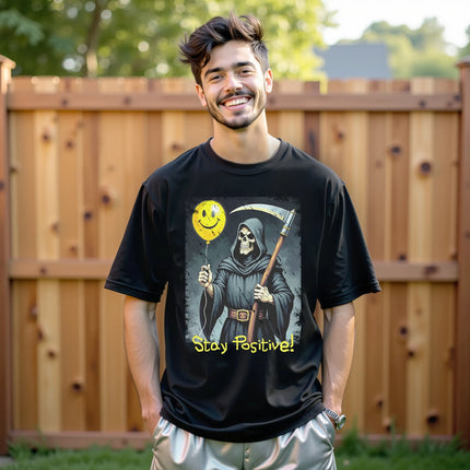 Model wearing black “Stay Positive” grim reaper t-shirt in a casual lifestyle setting, confident edgy look with dark humor graphic