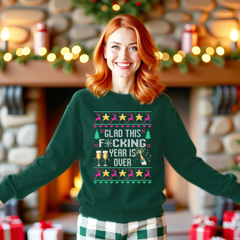 Female model wearing green funny New Year ugly sweater sweatshirt featuring ‘Glad This F*cking Year Is Over’ knitted-look lettering with champagne bottle, reindeer, and festive stars.