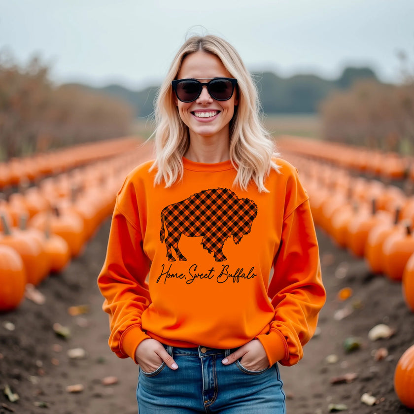 Woman wearing an orange Home Sweet Buffalo sweatshirt featuring a warm plaid buffalo silhouette and elegant script lettering, cozy fall fashion celebrating life in Buffalo NY.