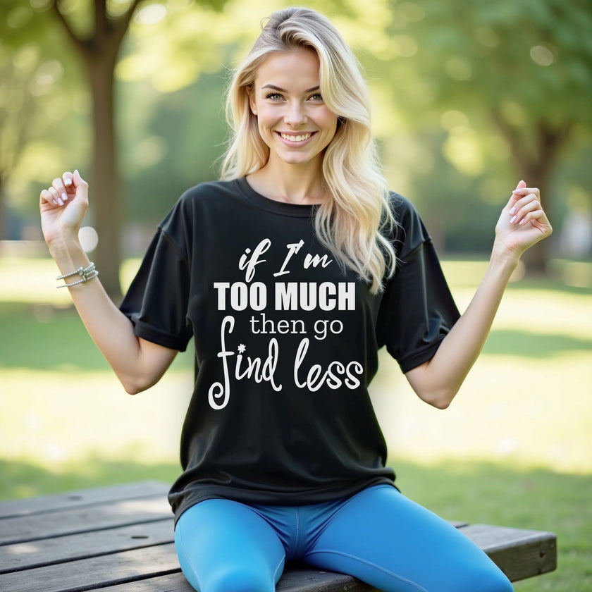 Female model wearing black “If I’m too much then go find less” t-shirt outdoors, layered typography design, confident sassy women’s casual outfit.