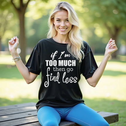 Female model wearing black “If I’m too much then go find less” t-shirt outdoors, layered typography design, confident sassy women’s casual outfit.