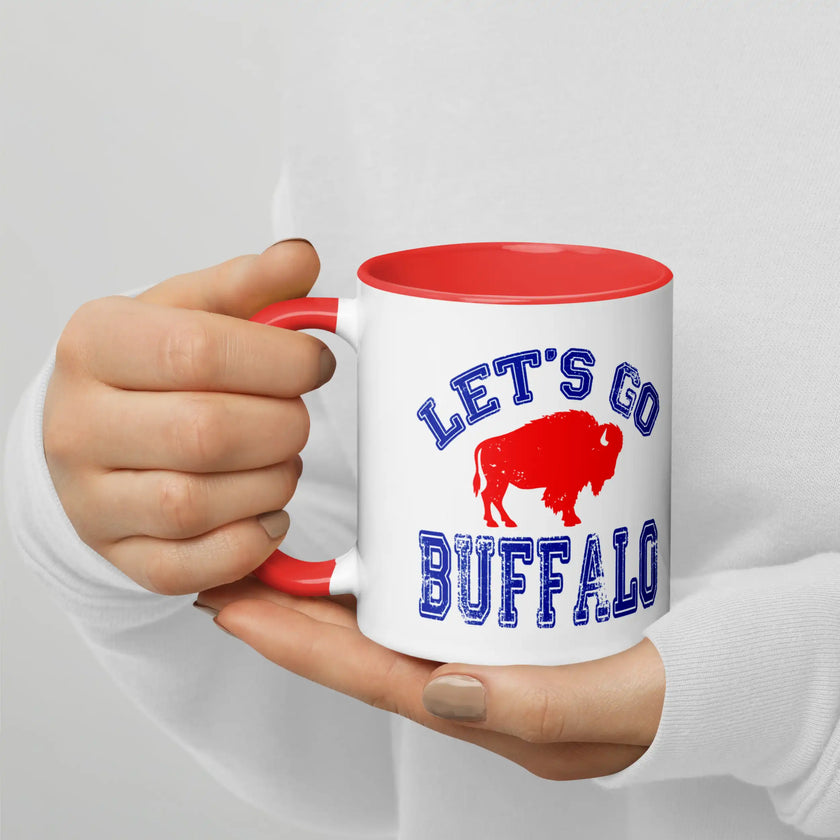 Hand holding white Let’s Go Buffalo football coffee mug showing blue distressed lettering and red buffalo logo during casual use.