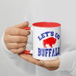 Hand holding white Let’s Go Buffalo football coffee mug showing blue distressed lettering and red buffalo logo during casual use.