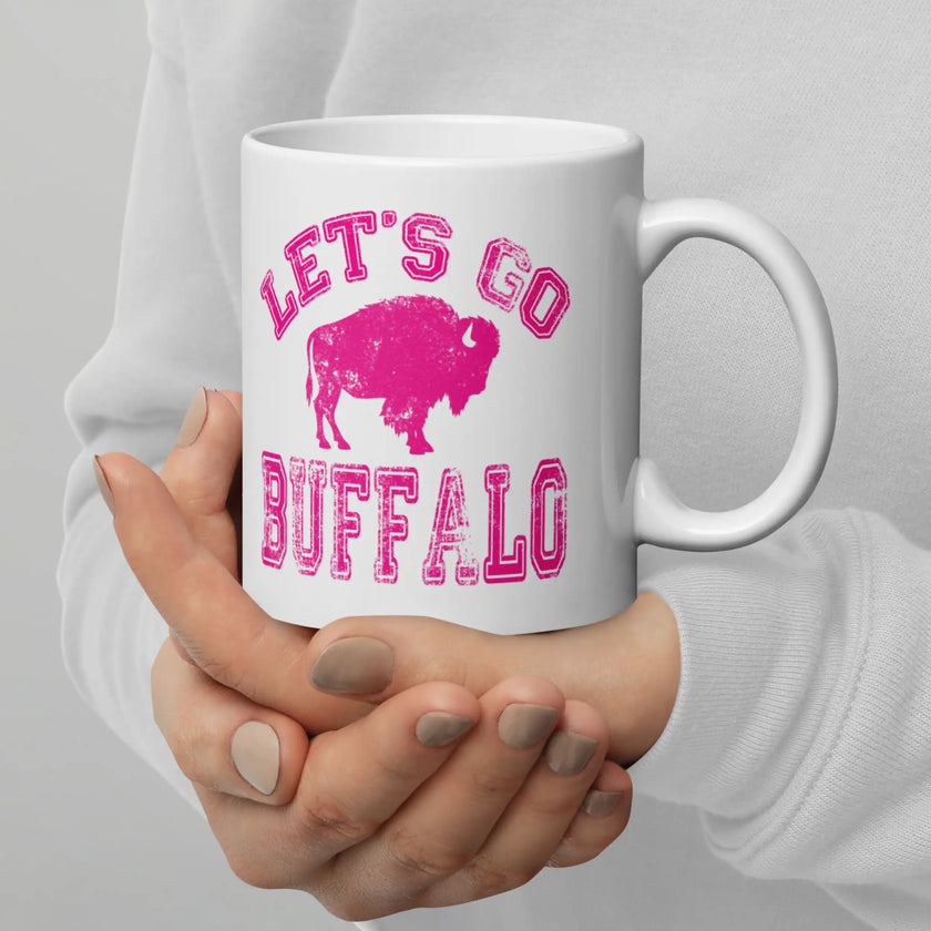 Close-up of white ceramic coffee cup with hot pink distressed ‘Lets Go Buffalo’ text and buffalo silhouette graphic in center, Buffalo football themed drinkware.