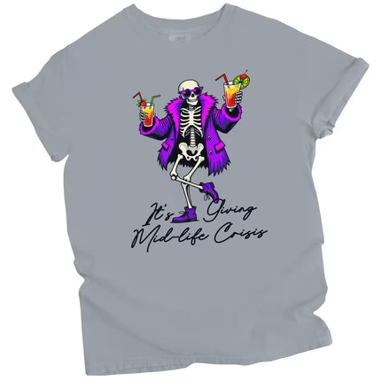 Gray “It’s Giving Mid-Life Crisis” t-shirt flat lay featuring playful skeleton with tropical drinks and sarcastic aging birthday message