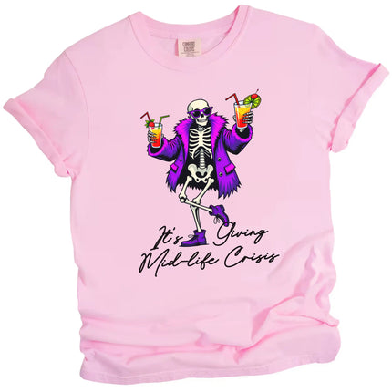 Pink “It’s Giving Mid-Life Crisis” t-shirt flat lay featuring dancing skeleton in purple fur coat holding tropical drinks, funny milestone birthday design