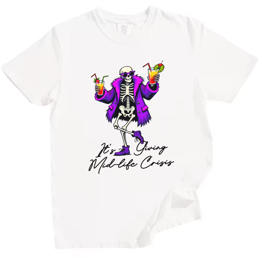 White “It’s Giving Mid-Life Crisis” t-shirt flat lay showcasing dancing skeleton with tropical drinks and bold sarcastic birthday graphic