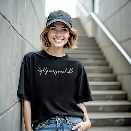 Model wearing black “Highly Unapproachable” t-shirt in a casual lifestyle setting, confident posture with sarcastic, unbothered energy
