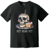 Black “Not Dead Yet” t-shirt flat lay showcasing skull with lit birthday candle, rainbow sprinkles, and cake slice, funny dark humor birthday design